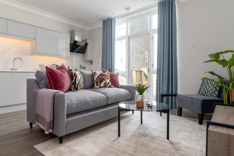 An array of images showcasing Urban Creation's luxury apartments. An apartment with open plan living, white kitchen. grey sofas lined with cushions, coffee table and accent chair